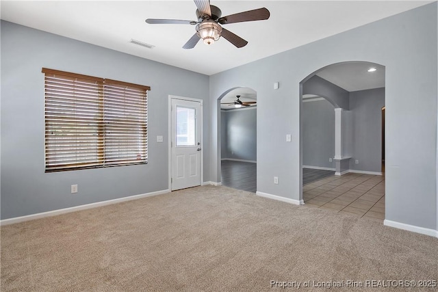 carpeted spare room featuring arched walkways, a ceiling fan, visible vents, and baseboards