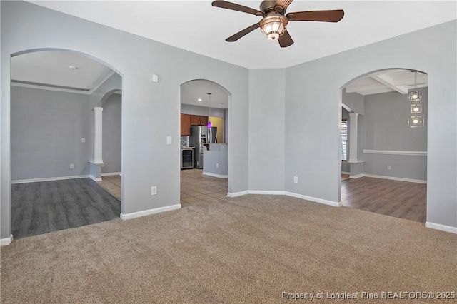 spare room with arched walkways, baseboards, carpet, beamed ceiling, and a ceiling fan