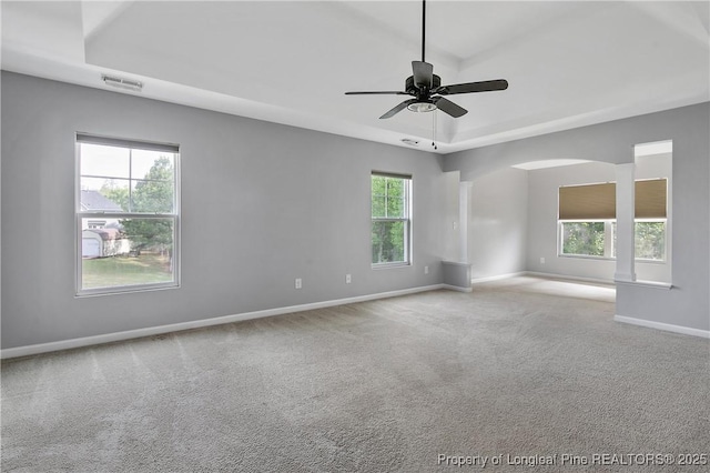 carpeted empty room with arched walkways, baseboards, visible vents, a ceiling fan, and a raised ceiling