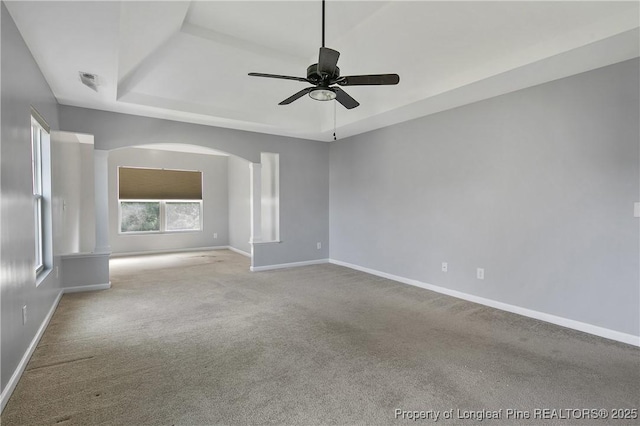 carpeted spare room with ceiling fan, baseboards, arched walkways, and a raised ceiling