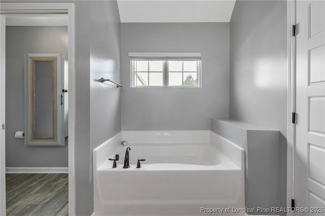 bathroom featuring wood finished floors, a garden tub, and baseboards
