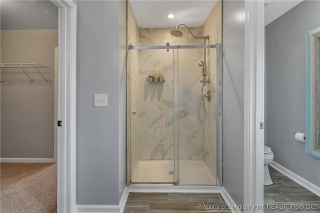full bath with a spacious closet, toilet, baseboards, and a marble finish shower