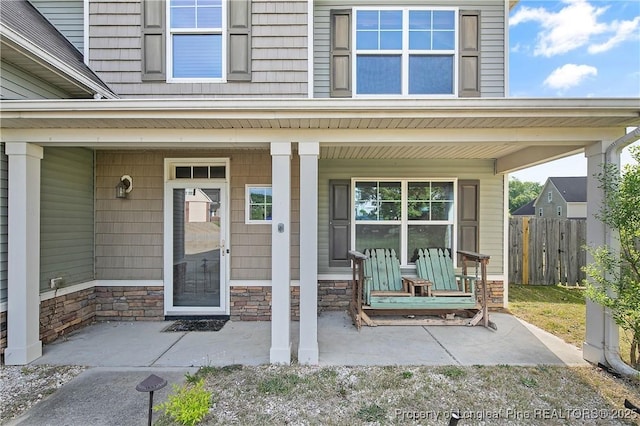 entrance to property featuring stone siding, covered porch, and fence
