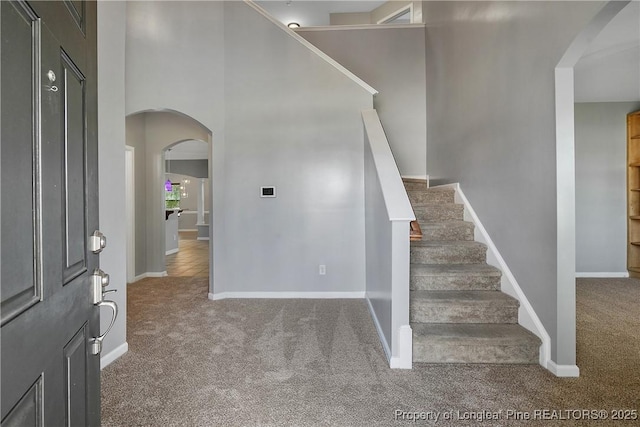 entrance foyer with a towering ceiling, arched walkways, carpet floors, baseboards, and stairs