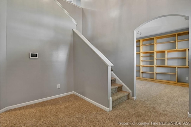 stairs featuring baseboards, arched walkways, and carpet