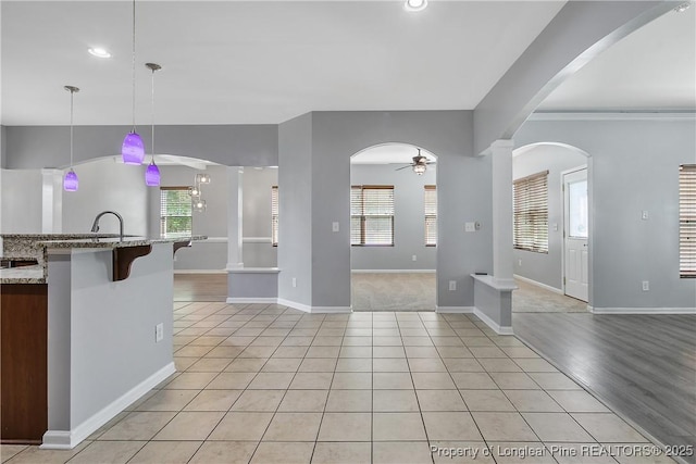 kitchen with light tile patterned floors, light stone countertops, pendant lighting, a kitchen bar, and ceiling fan