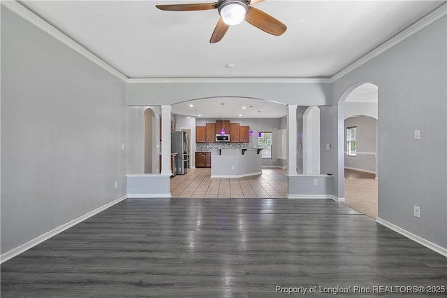 unfurnished living room featuring light wood-type flooring, ornamental molding, arched walkways, and ceiling fan
