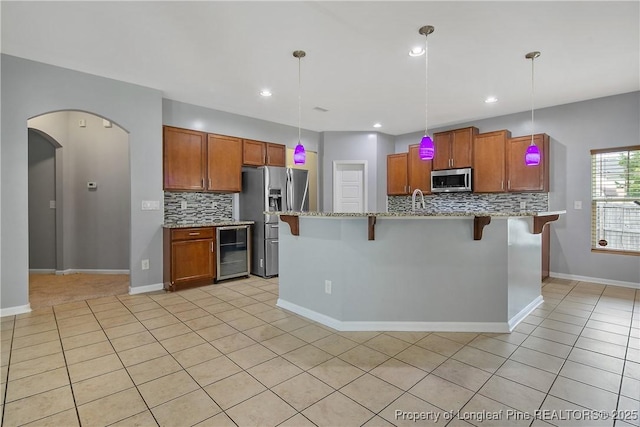 kitchen with stainless steel appliances, a kitchen bar, backsplash, light stone countertops, and beverage cooler