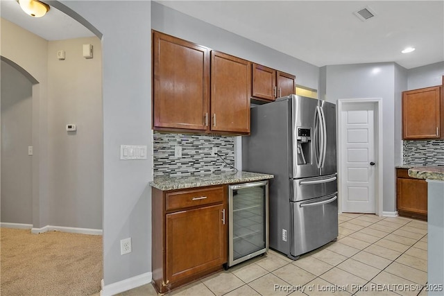 kitchen featuring tasteful backsplash, arched walkways, stainless steel refrigerator with ice dispenser, wine cooler, and visible vents