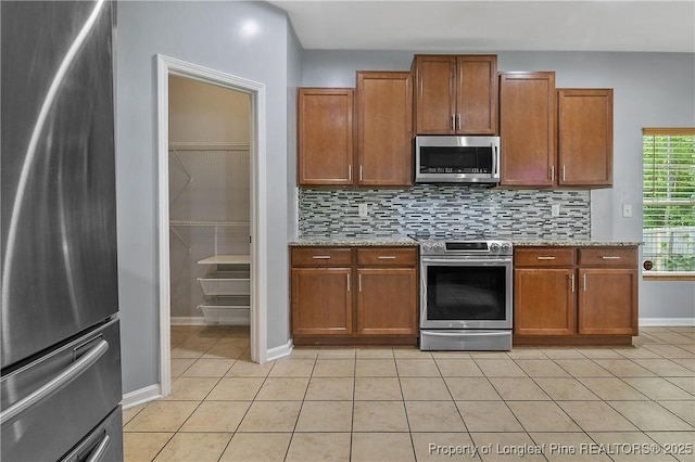 kitchen with stainless steel appliances, light tile patterned flooring, baseboards, decorative backsplash, and brown cabinetry