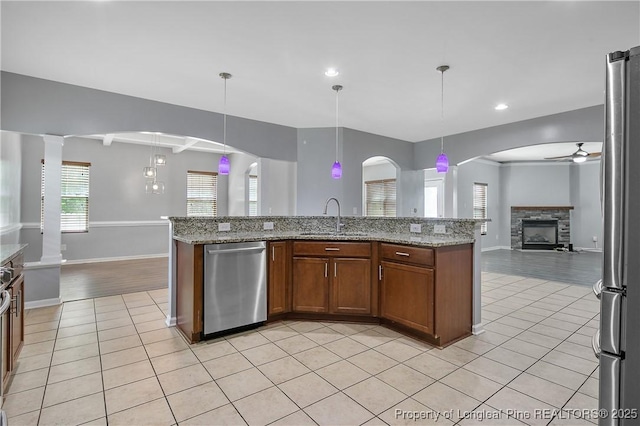 kitchen with a ceiling fan, a sink, open floor plan, light tile patterned flooring, and stainless steel appliances