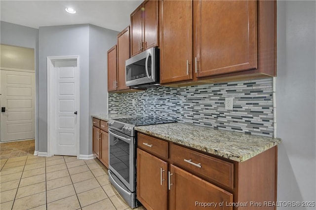 kitchen featuring brown cabinets, backsplash, light tile patterned floors, light stone countertops, and appliances with stainless steel finishes