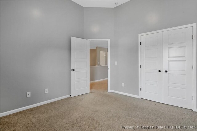 unfurnished bedroom featuring a closet, carpet flooring, baseboards, and a towering ceiling