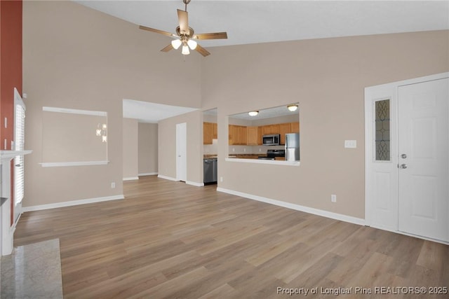 unfurnished living room with high vaulted ceiling, light wood finished floors, ceiling fan, and baseboards
