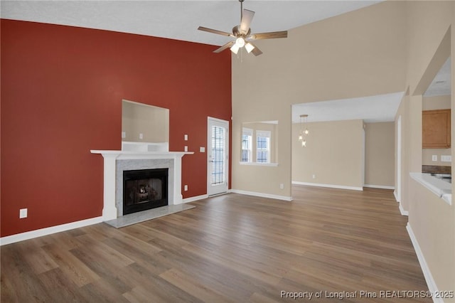 unfurnished living room featuring a high end fireplace, ceiling fan, wood finished floors, baseboards, and high vaulted ceiling