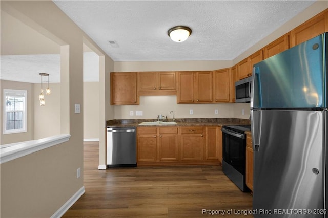 kitchen featuring stainless steel appliances, a sink, dark countertops, dark wood finished floors, and a textured ceiling