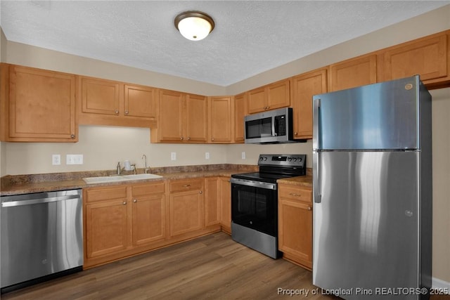 kitchen with stainless steel appliances, a sink, a textured ceiling, and wood finished floors