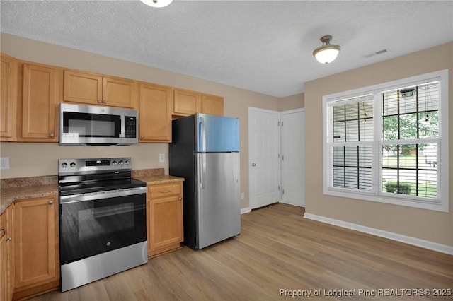 kitchen with appliances with stainless steel finishes, light wood-style floors, light countertops, baseboards, and light brown cabinetry