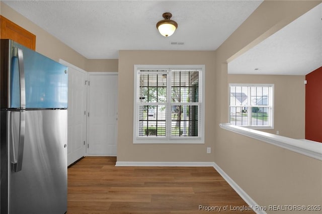 unfurnished dining area with wood finished floors, baseboards, and a textured ceiling