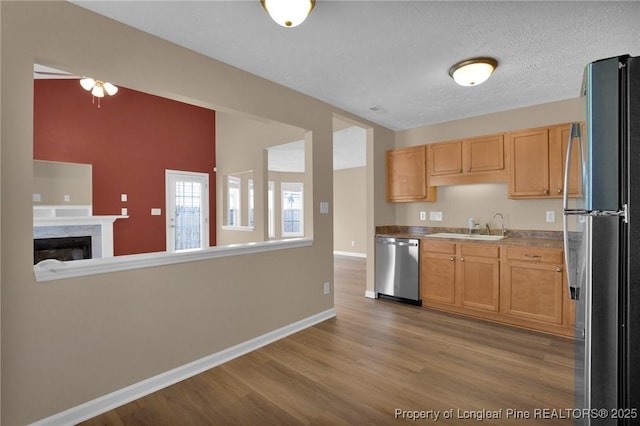 kitchen featuring appliances with stainless steel finishes, light wood-style flooring, baseboards, a sink, and a fireplace