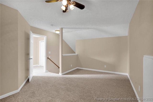 additional living space with carpet flooring, a ceiling fan, a textured ceiling, vaulted ceiling, and baseboards