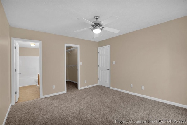 unfurnished bedroom featuring carpet, baseboards, a walk in closet, ensuite bathroom, and a closet