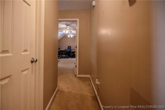 corridor with carpet flooring, a textured ceiling, and baseboards
