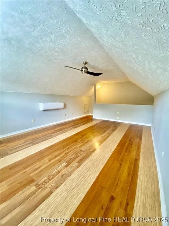 additional living space featuring wood finished floors, baseboards, a wall mounted air conditioner, a textured ceiling, and vaulted ceiling