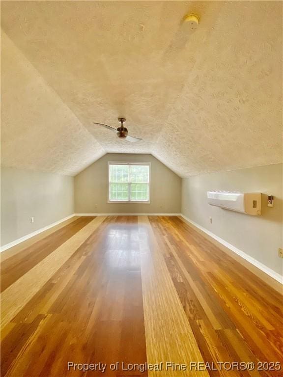 bonus room featuring baseboards, vaulted ceiling, a textured ceiling, and wood finished floors