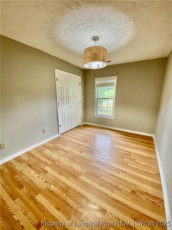 unfurnished bedroom featuring baseboards, a closet, light wood-type flooring, and a textured ceiling