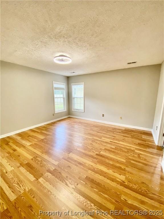 empty room featuring a textured ceiling, baseboards, and light wood-style floors