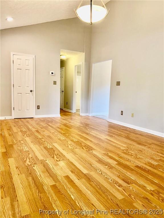 empty room with light wood-style floors, baseboards, and high vaulted ceiling