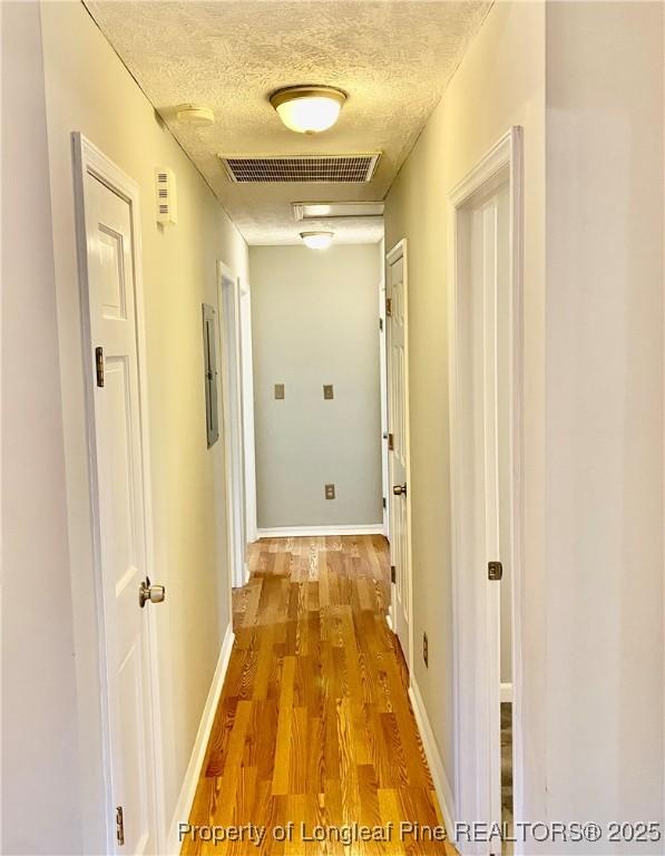 corridor featuring visible vents, baseboards, a textured ceiling, and wood finished floors