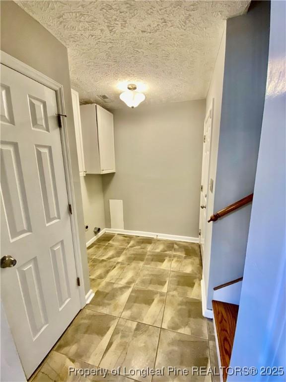 clothes washing area with cabinet space, a textured ceiling, and baseboards