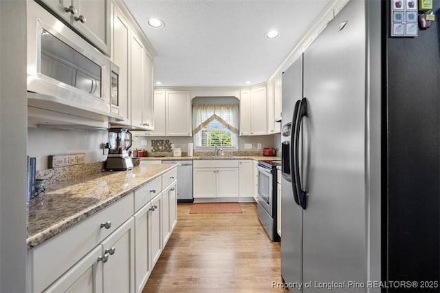 kitchen featuring appliances with stainless steel finishes, a sink, white cabinets, light wood finished floors, and recessed lighting