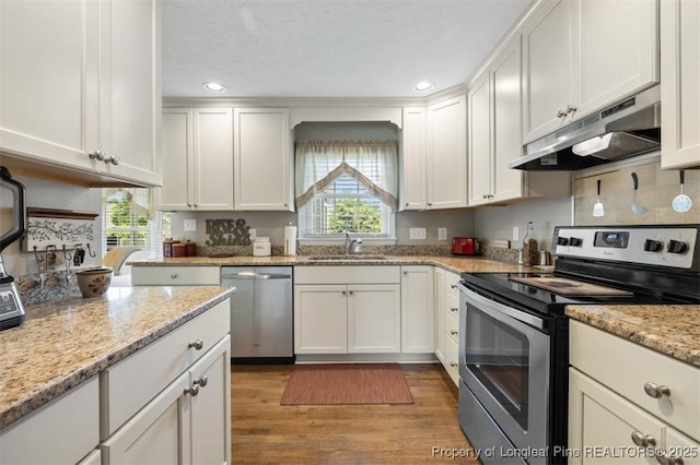 kitchen with appliances with stainless steel finishes, under cabinet range hood, a sink, white cabinetry, and wood finished floors