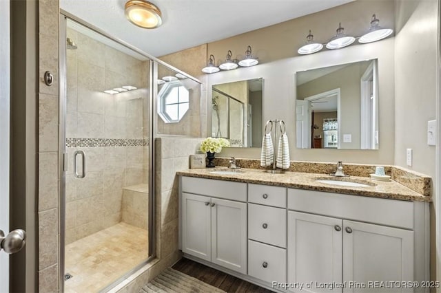 bathroom with double vanity, a stall shower, and wood finished floors