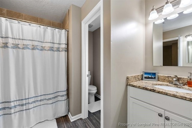 full bathroom featuring vanity, toilet, wood finished floors, a textured ceiling, and baseboards