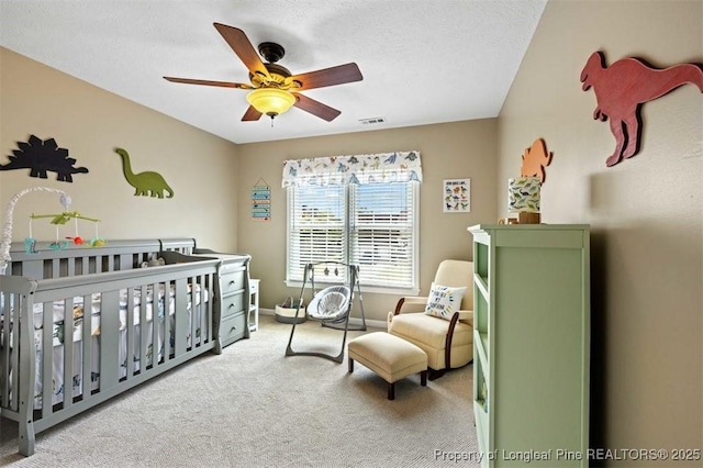bedroom featuring carpet flooring, a nursery area, baseboards, and a ceiling fan