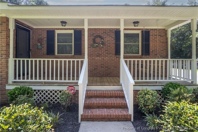 doorway to property featuring covered porch and brick siding