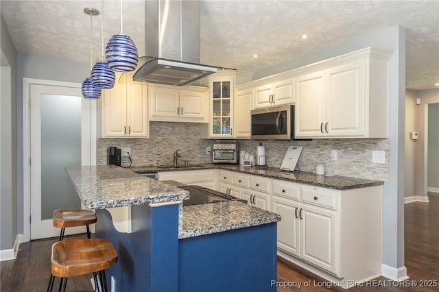 kitchen featuring stainless steel microwave, island range hood, decorative backsplash, dark wood-style flooring, and a textured ceiling