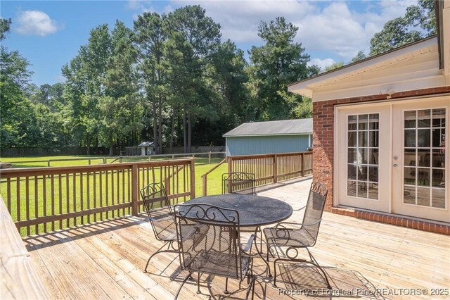 deck featuring outdoor dining space, a fenced backyard, view of wooded area, and an outbuilding