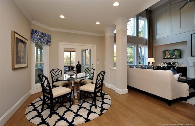 dining area featuring crown molding, decorative columns, light wood-type flooring, and a healthy amount of sunlight