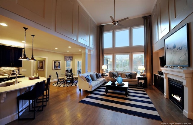 living room with ceiling fan, dark hardwood / wood-style flooring, sink, a towering ceiling, and ornamental molding