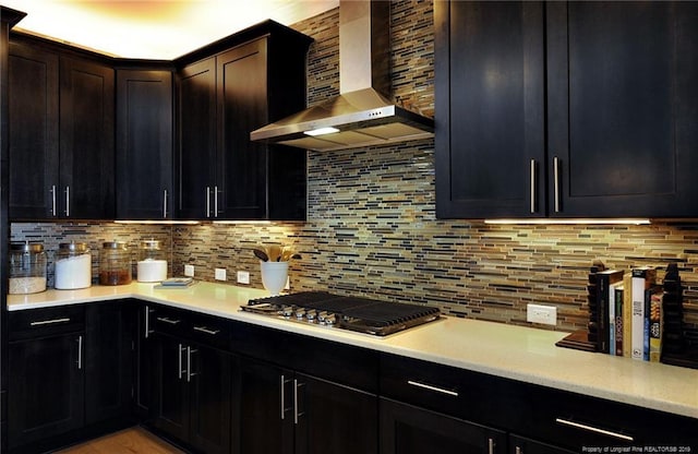 kitchen featuring dark brown cabinets, backsplash, wall chimney range hood, and stainless steel gas cooktop