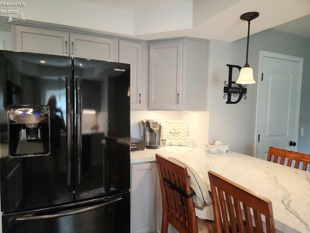 kitchen with light stone counters, a breakfast bar, gray cabinetry, decorative light fixtures, and black fridge with ice dispenser