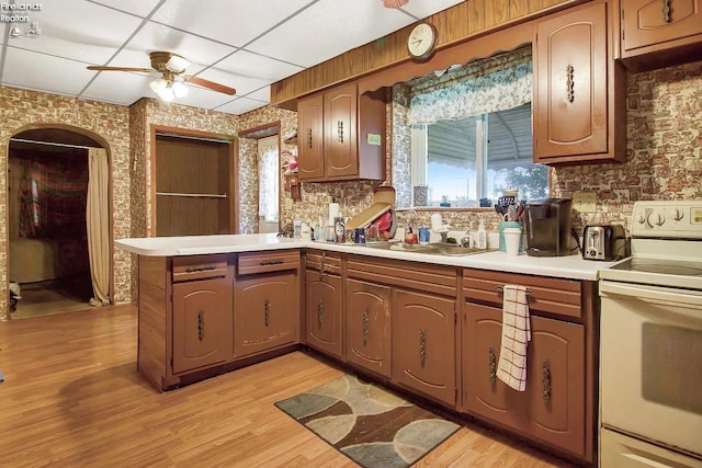 kitchen featuring ceiling fan, sink, kitchen peninsula, white range with electric cooktop, and light hardwood / wood-style floors