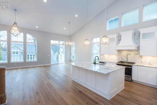 kitchen featuring custom range hood, open floor plan, stainless steel gas stove, white cabinetry, and an island with sink