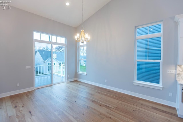 spare room with high vaulted ceiling, an inviting chandelier, light wood-style flooring, and baseboards