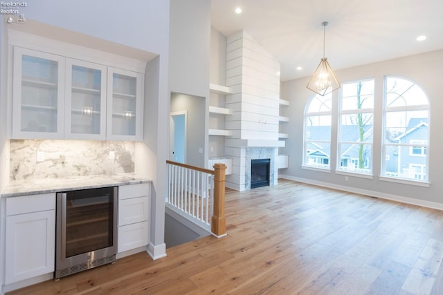 kitchen with light stone counters, wine cooler, glass insert cabinets, light wood-style floors, and white cabinets